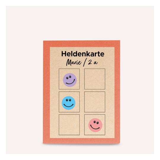 Изображение показывает карточку с заголовком «Heldenkarte» с местом для наклеек. Она имеет четыре ячейки, три из которых заполнены смайликами фиолетового, синего и розового цветов, и одна пустая ячейка.