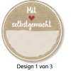 Изображение показывает круглую этикетку с текстом «Mit ❤️ selbstgemacht» (С любовью, сделано вручную) и пустым пространством под ним. Дизайн находится на текстурированном, бежевом фоне с декоративными рамками. Также имеется примечание «Design 1 von 3» (Дизайн 1 из 3).