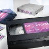 Изображение содержит видеокассету VHS с надписью "beEvents SALES MEETING 2014" рядом с другими устройствами для хранения медиа, такими как дискеты и картридж для хранения данных, все с аналогичным брендингом.