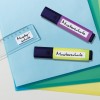 Изображение содержит два текстовыделителя с надписью 'Mustersschule' и прозрачную линейку на синем фоне с несколькими листами цветной бумаги.
