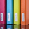 Изображение показывает ряд цветных папок для файлов с ярлыками на немецком языке. Ярлыки гласят «Rechnungen» (Счета-фактуры), «Kunden» (Клиенты), «Lieferscheine» (Товарные накладные) и «Korrespondenz» (Переписка), расположенных на отражающей поверхности.