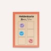 Изображение показывает карточку с заголовком «Heldenkarte» с местом для наклеек. Она имеет четыре ячейки, три из которых заполнены смайликами фиолетового, синего и розового цветов, и одна пустая ячейка.